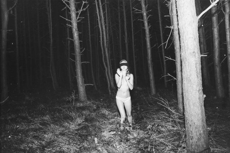 Blindfolded sensuous topless woman against trees at forest during night