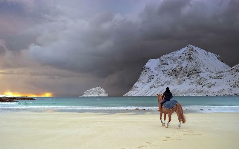 Man riding horse with sea and snow covered cliffs in background