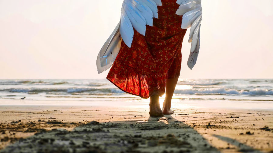 Low section of woman walking at beach against sky