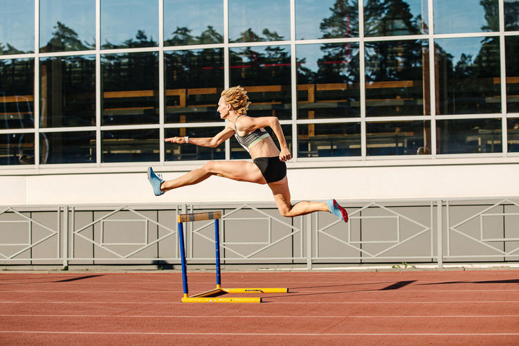 Woman athlete runnner running hurdles in summer athletics competition