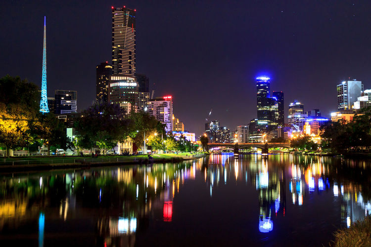 Illuminated buildings with reflection in yarra river against sky at night
