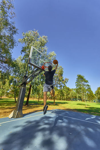 Rear view of man putting ball in basketball hoop against clear sky