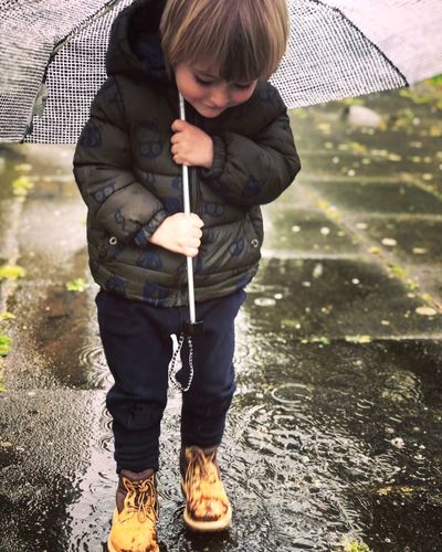 Full length of boy holding umbrella while standing on wet road