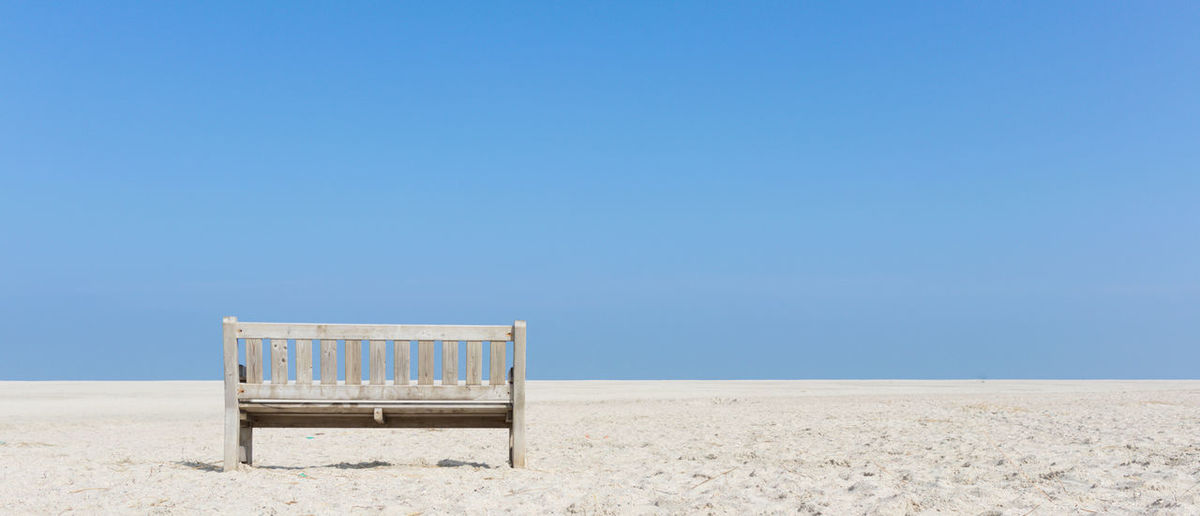 Empty deck chairs on sand against clear blue sky