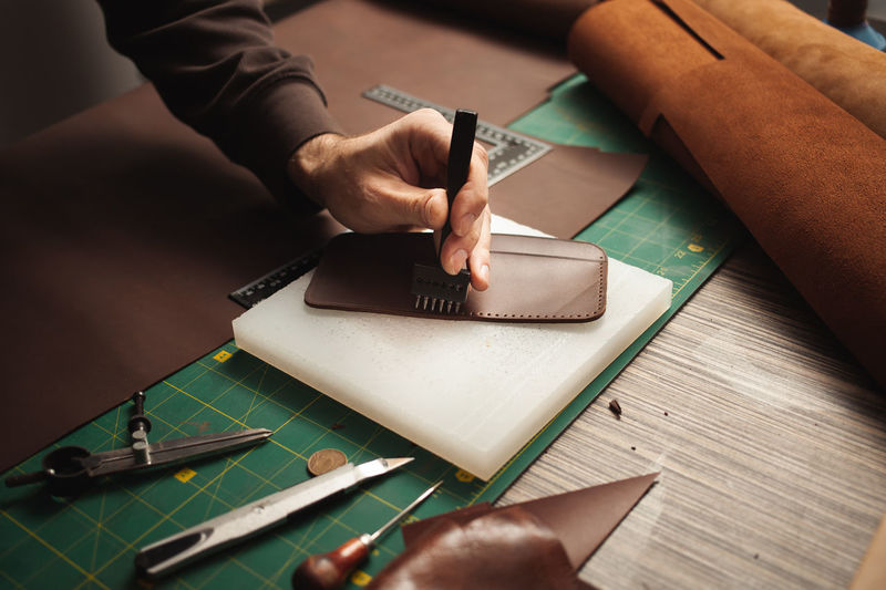 Leatherworker punches holes. tanner works with leather, small business, production.