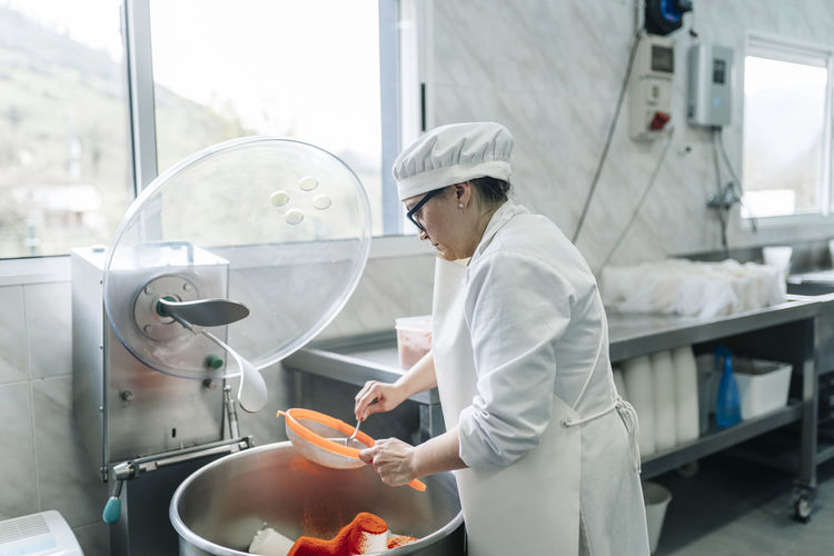 Female cheese expert using strainer in factory
