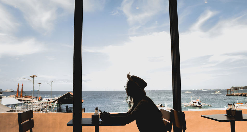 Man sitting on table in restaurant by sea against sky