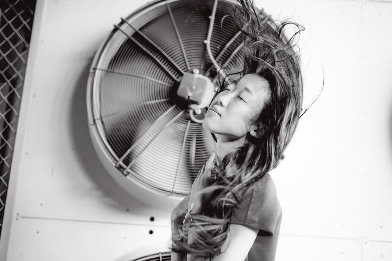 Young woman with tousled hair standing against exhaust fans