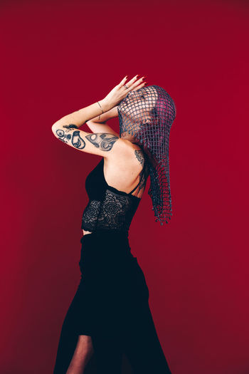 Young woman wearing dress and scarf while posing against red background