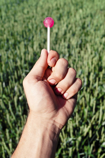 Cropped image of hand holding lollipop candy on field