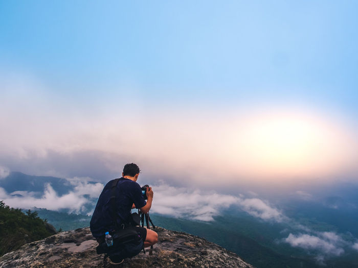 Man sitting on mountains against sky during sunset
