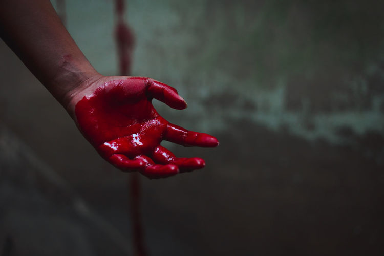 Cropped hand of person with blood against wall