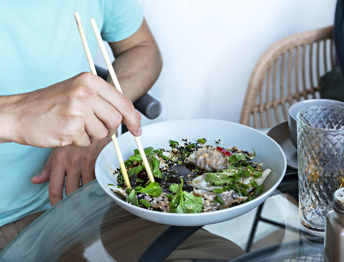 Man eating chopsticks vegan food jiaozi with tofu , vegetables in soy sauce , parsley chinese dish 