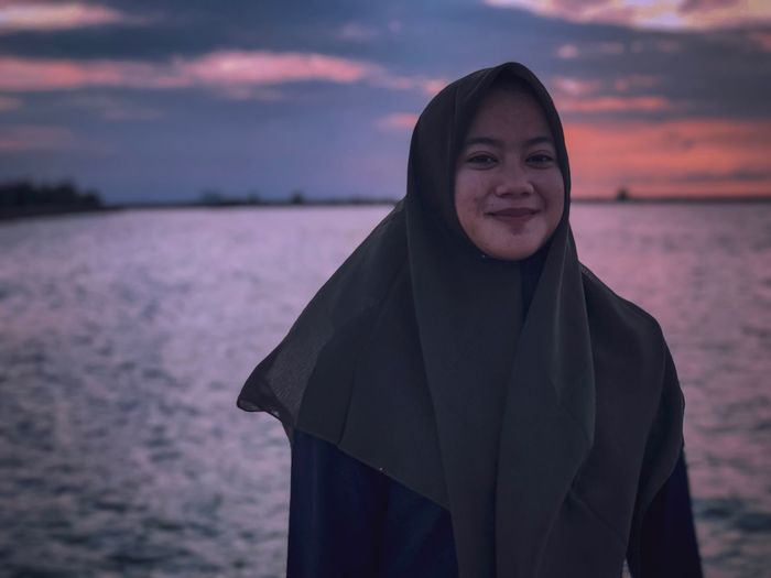 Portrait of smiling woman standing against sea during sunset