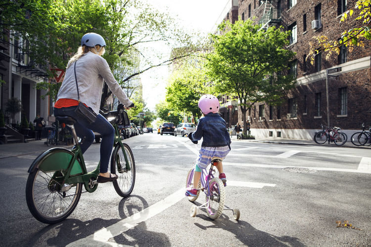 Rear view of mother and daughter riding bicycles on street