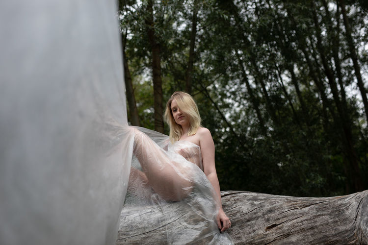 Young naked woman sitting on tree trunk in forest