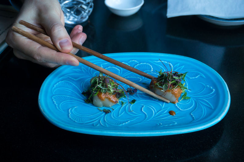 Eating raw scallop dish served with herbs and sauce with chopsticks. japanese restaurant background
