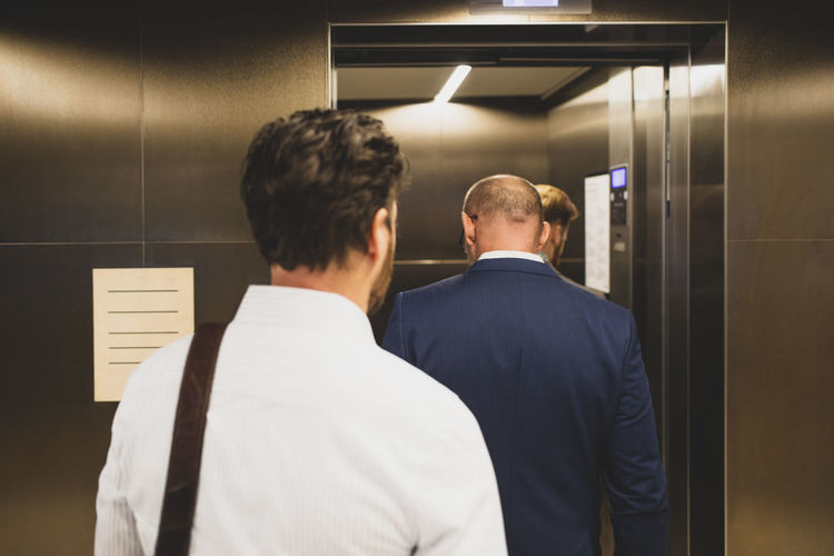 Rear view of business people walking inside elevator