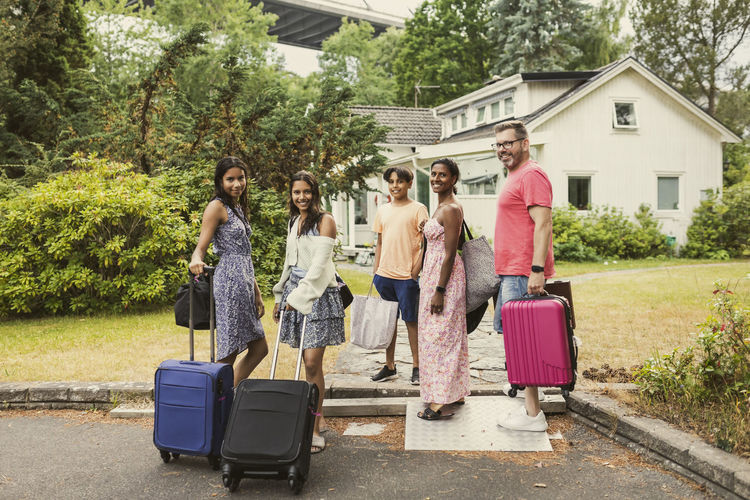 Portrait of happy multiracial family standing with luggage in front of house