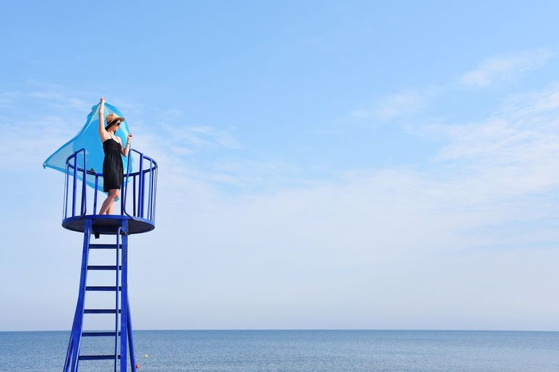 Young woman holding scarf on lookout tower by sea against sky