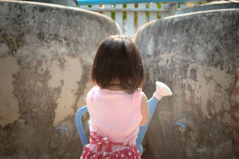 Rear view of girl with watering can against wall