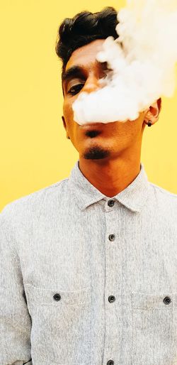 Portrait of young man smoking against yellow background