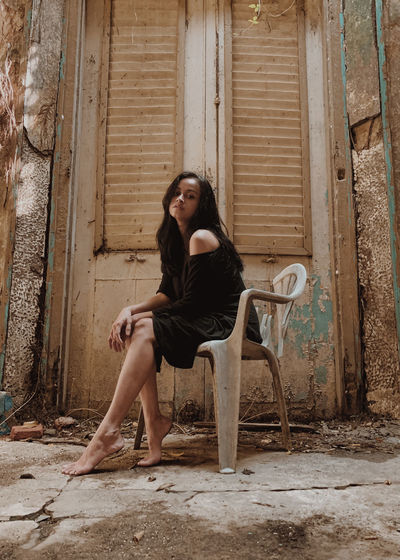 Portrait of young woman sitting on old abandoned house