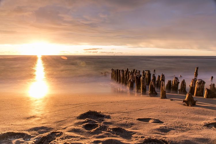 Wooden posts at beach against cloudy sky during sunset