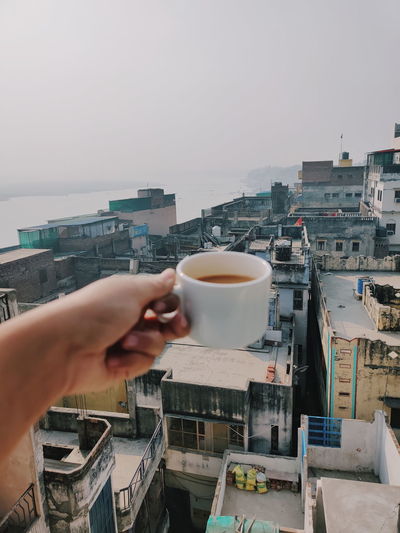 Man holding coffee cup and cityscape against sky