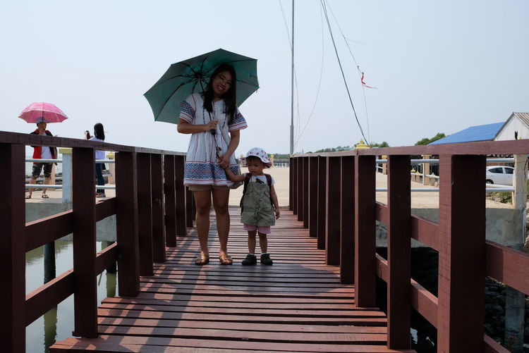 Full length of mother and daughter standing on pier against sky