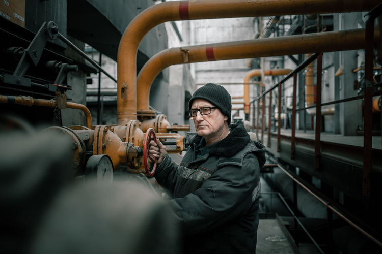 Senior man examining pipes in factory