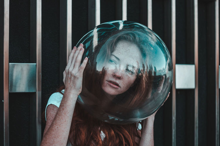 Close-up of thoughtful young woman wearing glass helmet in head against metallic railing