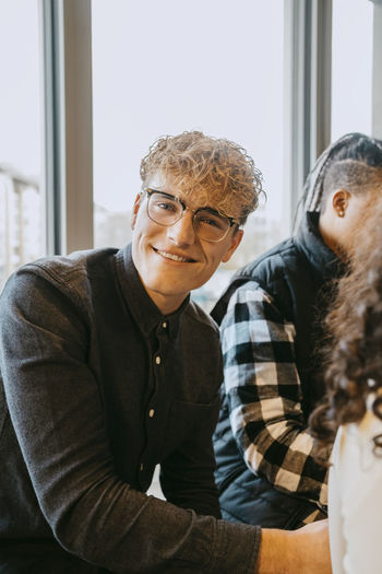 Portrait of smiling blond man wearing eyeglasses sitting at cafeteria in university