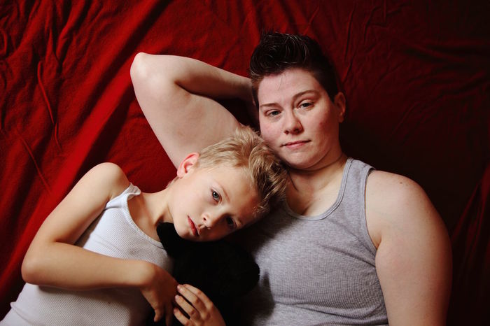 Portrait of mother and son with puppy lying on red fabric