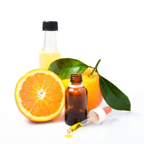 Close-up of orange fruits with bottle against white background