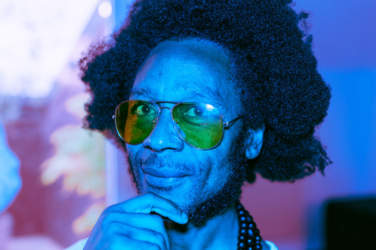 Portrait in blue neon light of an african american brazilian man with sunglasses and pupils dilated 