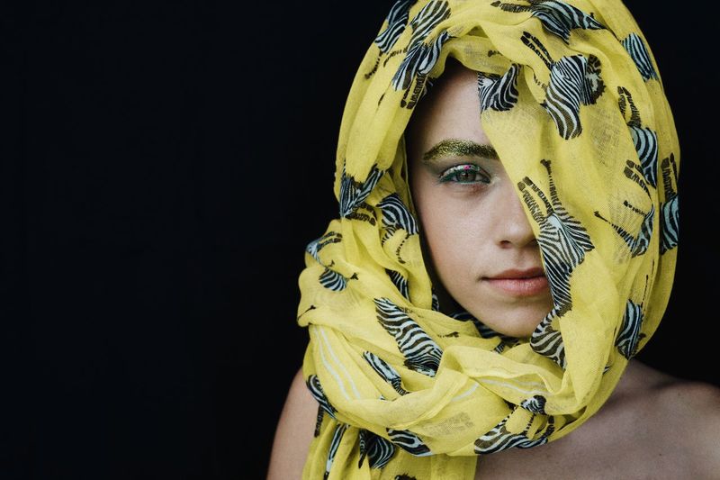 Portrait of young woman wearing yellow headscarf against black background