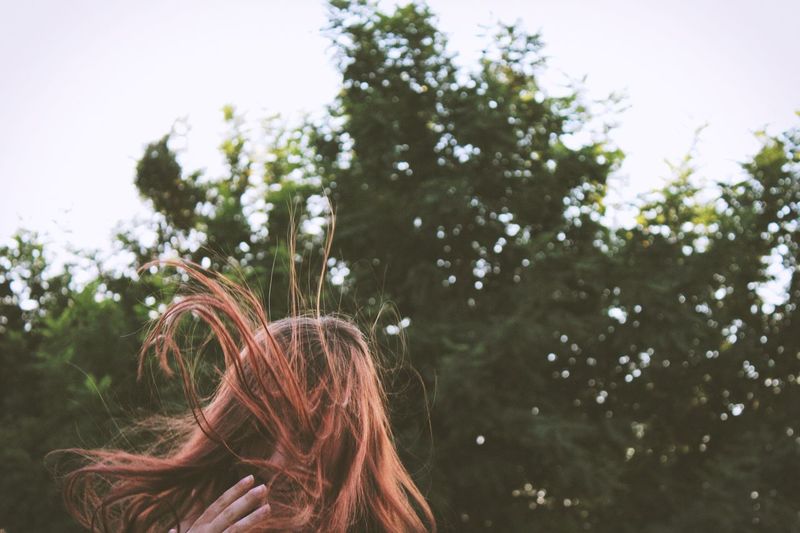 Low angle view of woman with tousled brown hair against trees