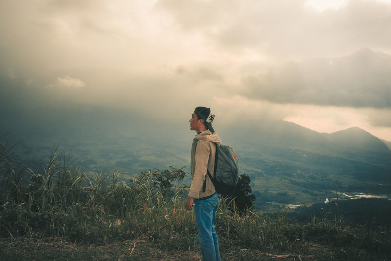 Young man standing on mountain against sky