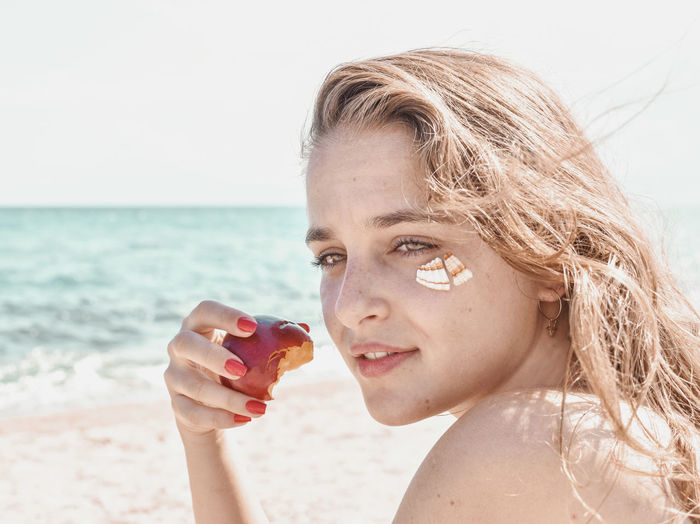 Portrait of woman holding sunglasses at beach against sky