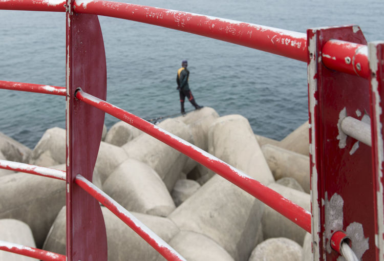Man standing on concrete block against sea seen through railing