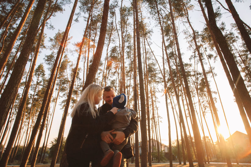 Happy young family standing in forest at sunset in autumn