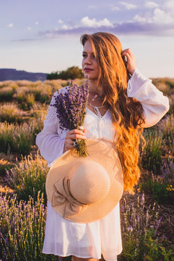 Beautiful woman standing on field by flowering plants against sky