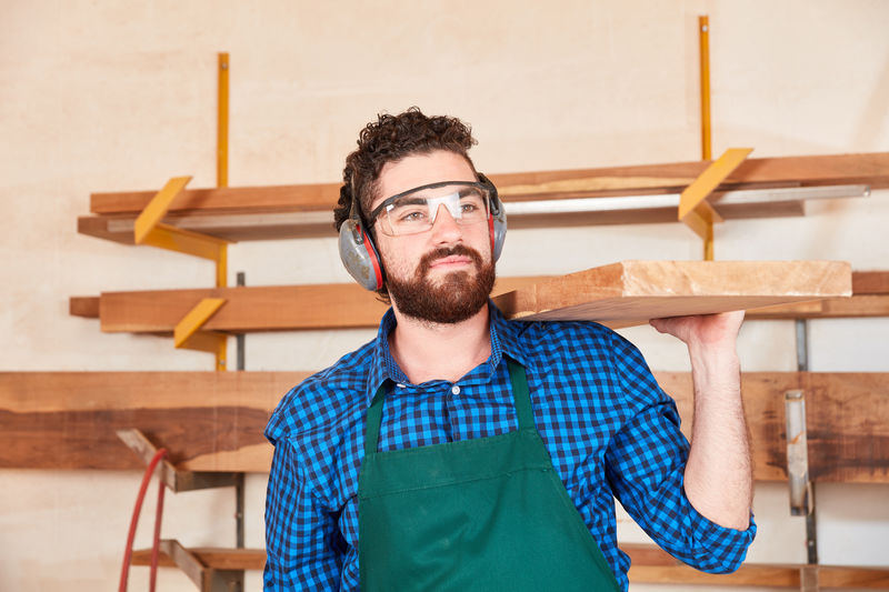 Young man carrying timber on shoulder at workshop