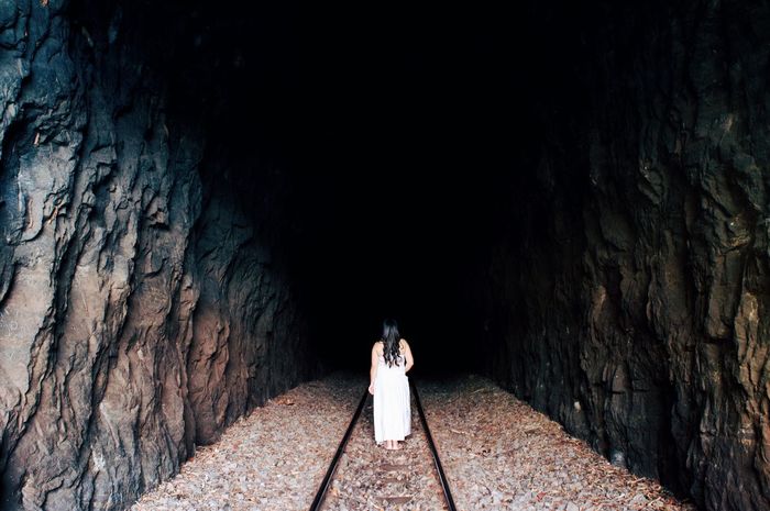 Rear view of woman standing on railroad track in tunnel