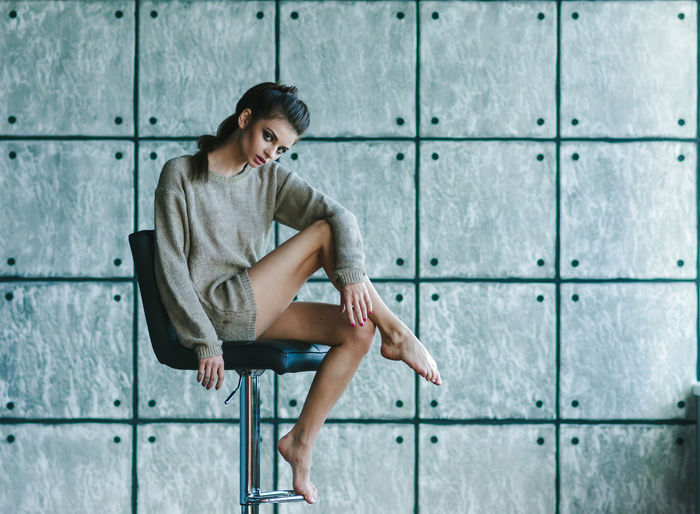 Full length of a young woman sitting on wall