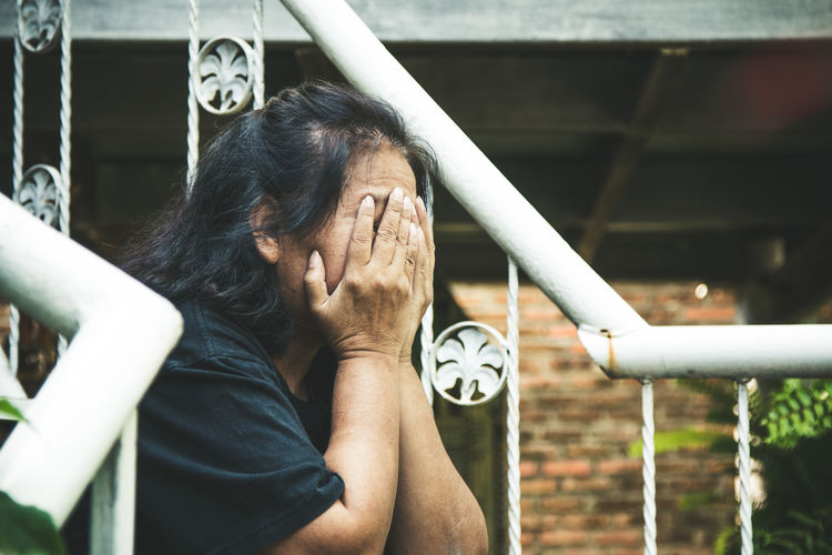 The old woman place her hands on face and be depressed feeling while sitting on stairs