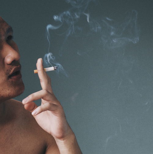 Close-up of man smoking cigarette against wall