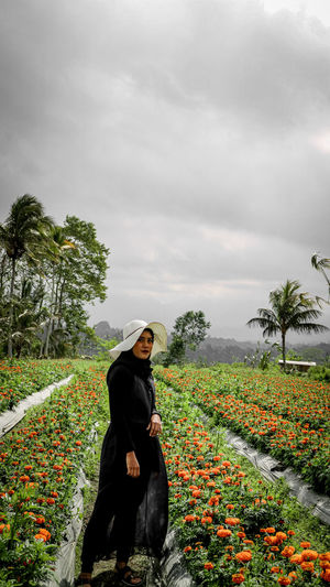 Full length of young woman standing on flowering field