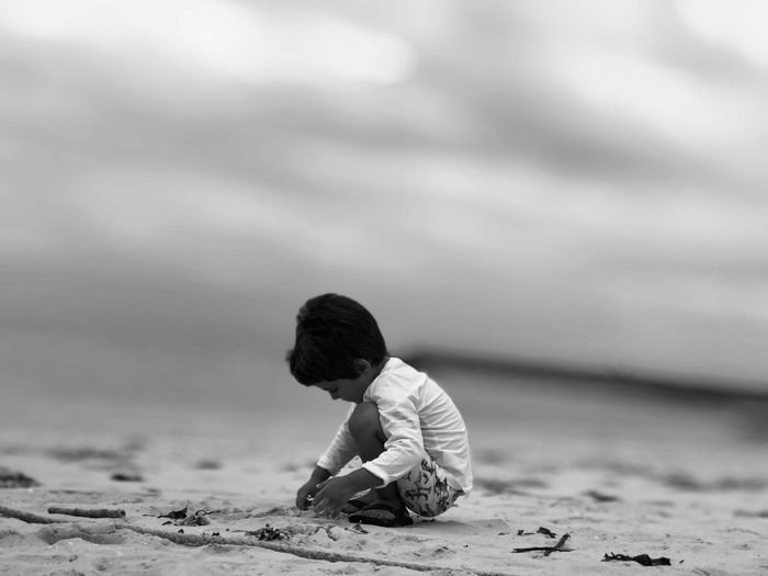 Side view of boy playing on sandy beach against cloudy sky